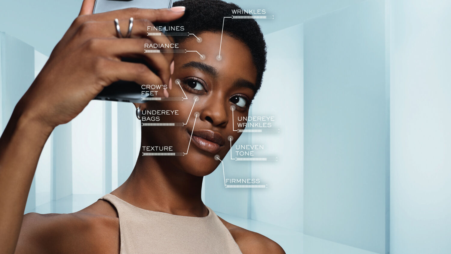 A young woman takes a selfie while labels point to various skin concerns, including wrinkles, fine lines, radiance, crow's feet, under-eye bags, texture, uneven tone, and firmness.