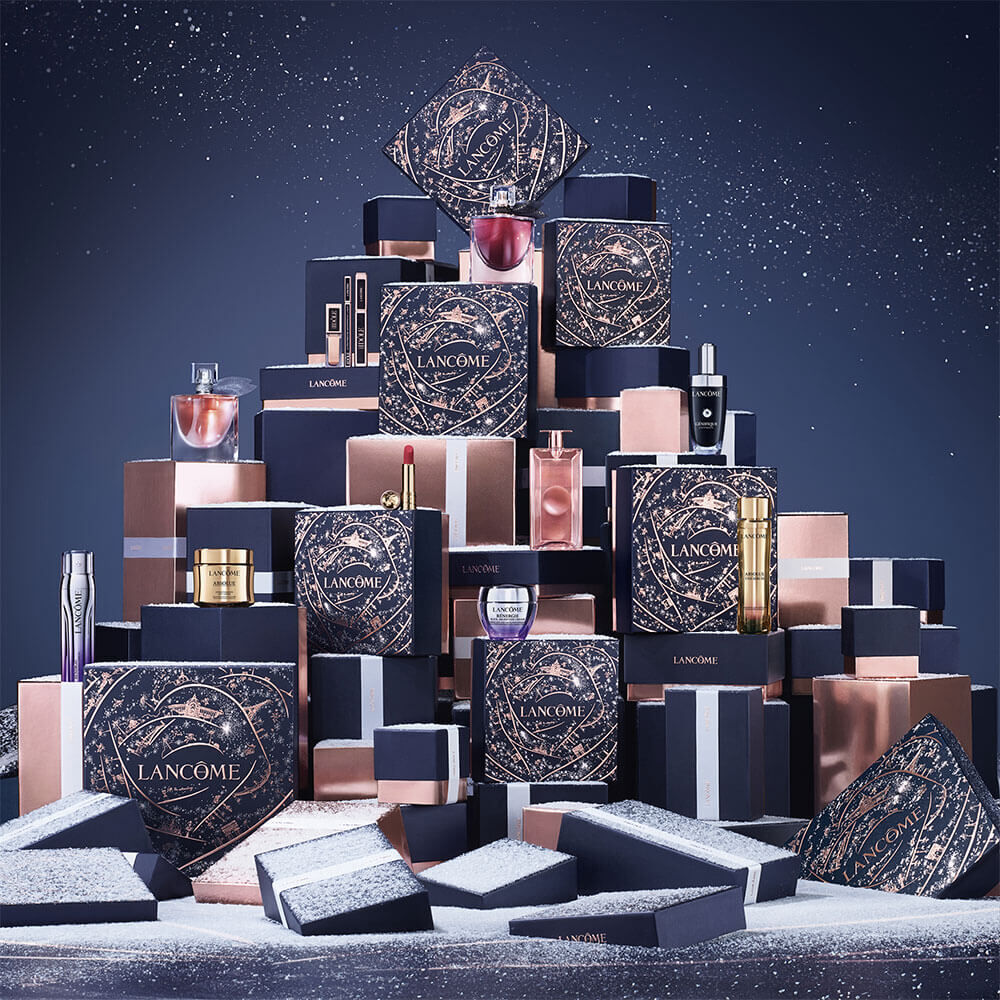 An elegantly arranged display of Lancome gift boxes and cosmetic products, set against a snowy background.
