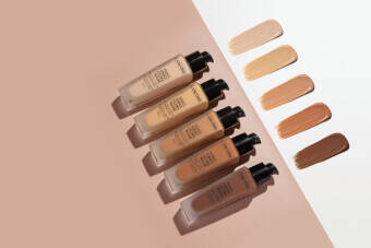 Five bottles of foundation in varying shades are displayed on a neutral background, alongside swatches of the same shades.