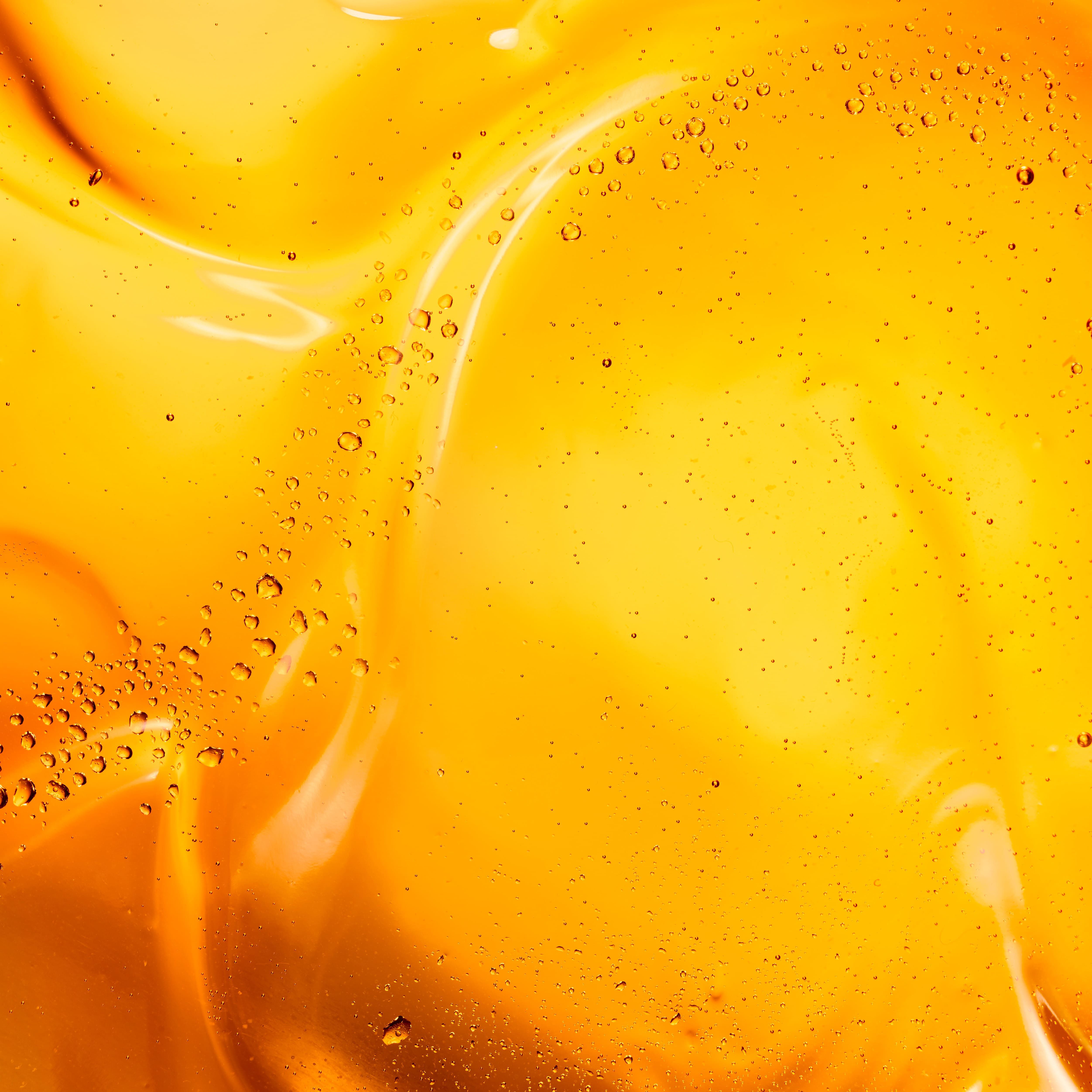 Abstract close-up of a vibrant orange liquid with swirling patterns and bubbles, creating a dynamic and fluid appearance.
