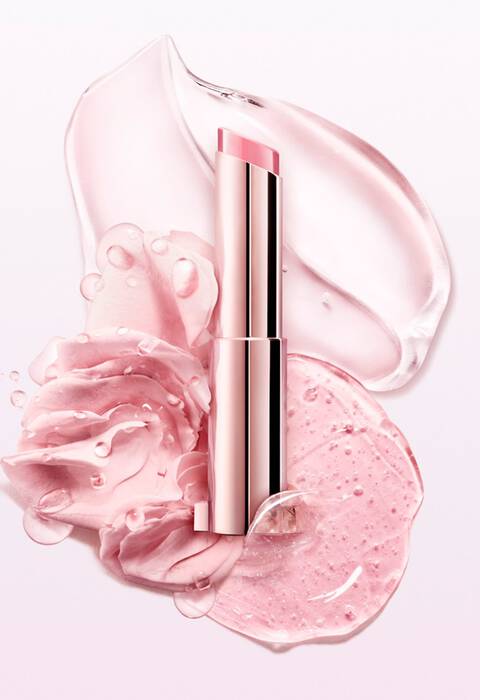 A pink lipstick tube rests on a smooth, translucent gel and rose petals, creating a fresh and elegant beauty composition.