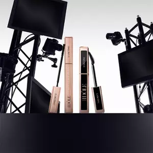 A sleek display featuring Lancome mascara products, surrounded by cameras and studio equipment, set against a gradient background.