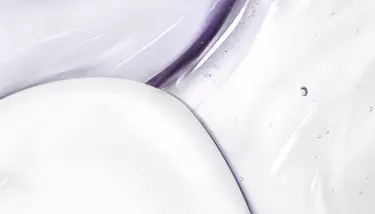 A macro shot of swirled white cream and clear gel with purple undertones and small bubbles.