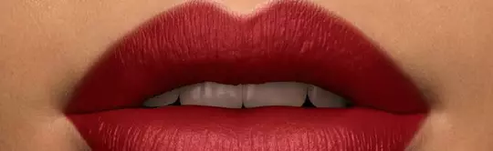 Close-up of a person's lips painted in bold red lipstick, with a neutral skin tone in the background.