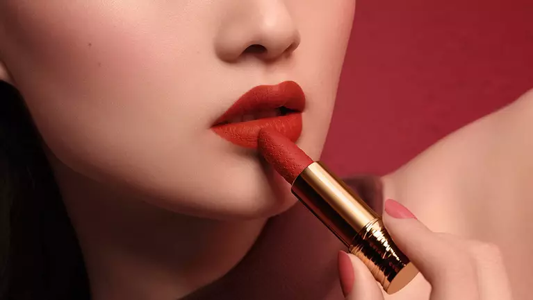 A close-up of a woman's lips being accentuated with a bold red lipstick against a rich red background.