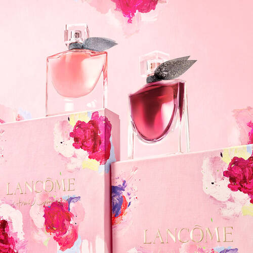 Two elegant Lancome perfume bottles in pink and deep red on floral-themed boxes against a soft pink background.