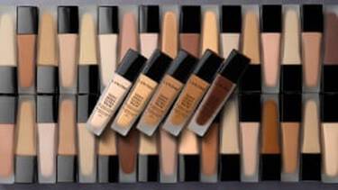 A wide array of Lancome foundation bottles in various shades, forming a textured pattern, with five bottles angled across the center.
