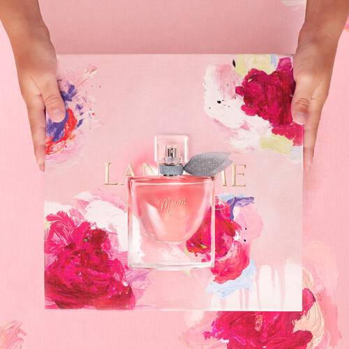 A hands holding a pink floral bottle of Lancome perfume on a vibrant, painted floral background.