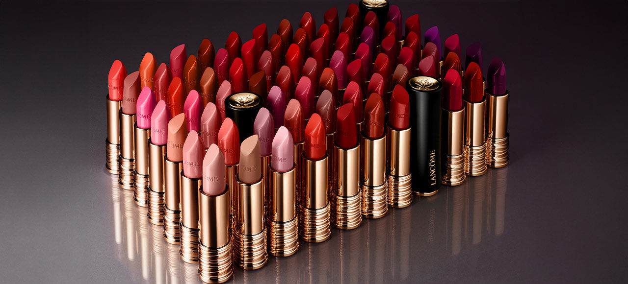 A collection of various shades of lipsticks arranged in rows, featuring vibrant reds, pinks, and purples, with gold and black packaging.