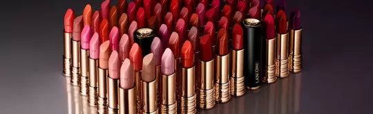 A collection of various shades of lipsticks arranged in rows, featuring vibrant reds, pinks, and purples, with gold and black packaging.