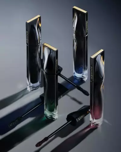 Four sleek, modern perfume bottles are arranged in a triangular formation on a dark surface, casting subtle shadows. The bottles have shiny metal caps and feature a gradient of colors from blue to green to red, enhancing their elegant appearance.