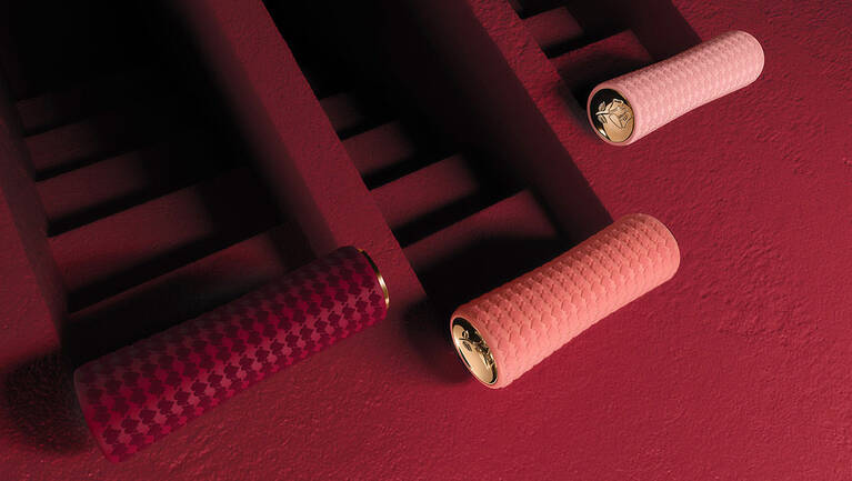 Three textured bike grips in pink and burgundy are mounted on a dark red wall, showcasing a modern design aesthetic.