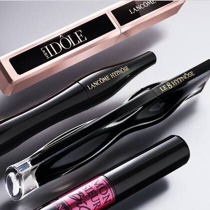 A collection of four Lancome mascara tubes arranged horizontally on a gradient background.