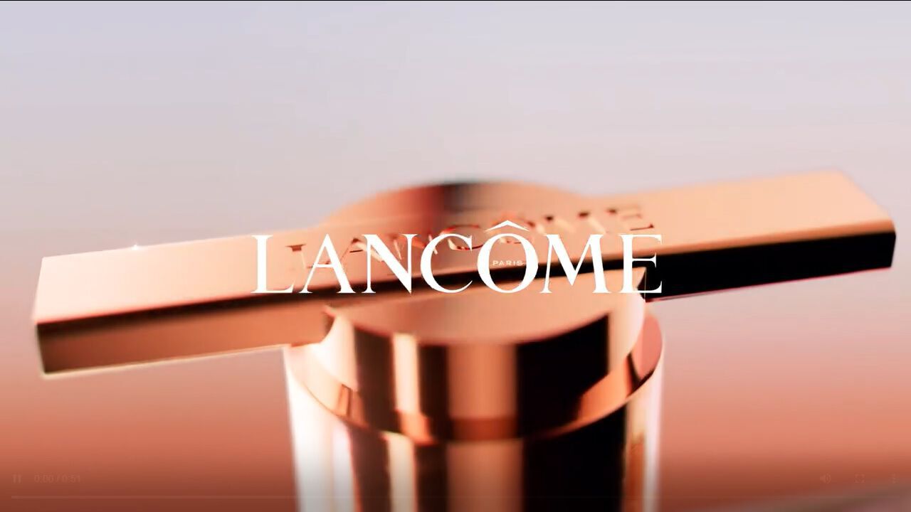Close-up of a luxurious, cylindrical beauty product with a metallic cap, featuring the Lancome logo prominently displayed in the center.