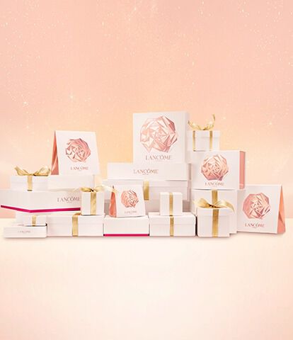 A collection of elegant gift boxes from Lancome, stacked creatively with soft pink and gold accents against a light pink background.