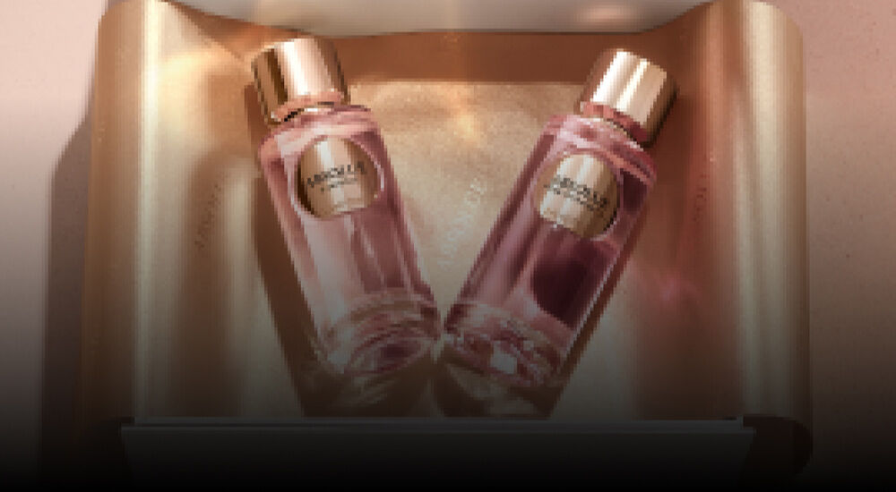 A gift box partially open, revealing two elegant perfume bottles with gold accents, nestled in a metallic gold tissue paper.