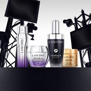 A display of Lancome skincare products, including bottles of Genifique Ultimate, Renergie Multi-Action Cream, and Absolue, arranged stylishly with a backdrop of studio lighting equipment.
