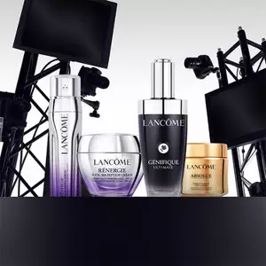 A display of Lancome skincare products, including bottles of Genifique Ultimate, Renergie Multi-Action Cream, and Absolue, arranged stylishly with a backdrop of studio lighting equipment.