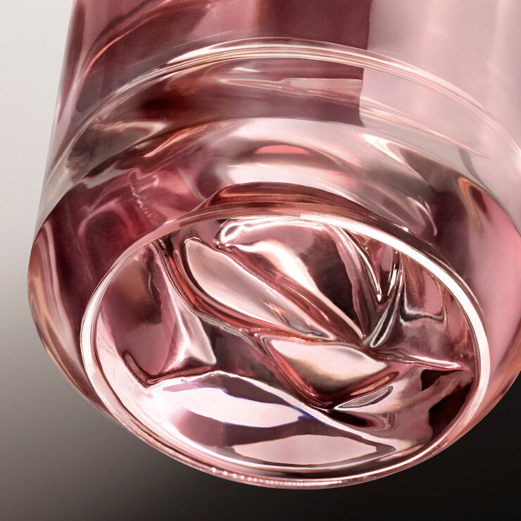 Close-up of the bottom of a clear glass with a soft pink hue, featuring a swirling design in the glass.