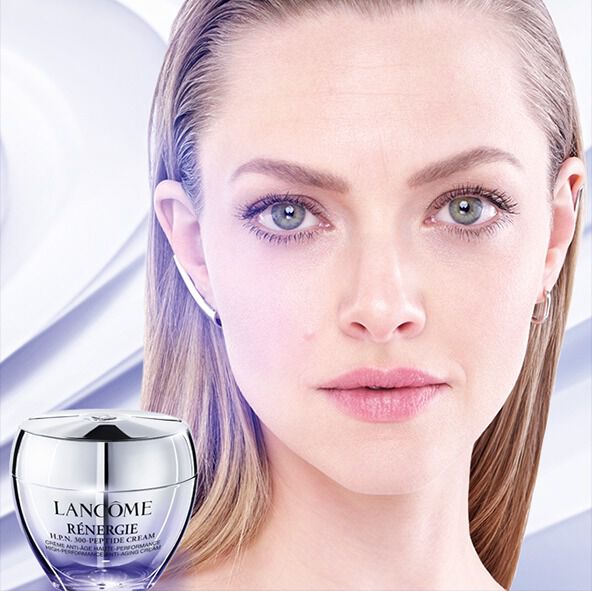 A close-up of a woman's face with clear skin, next to an open jar of cream on a light, flowing background.