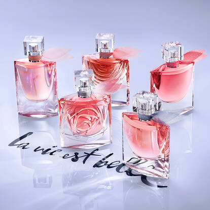 A collection of five elegant perfume bottles displayed on a reflective surface, accompanied by the phrase "la vie est belle" in artistic lettering.