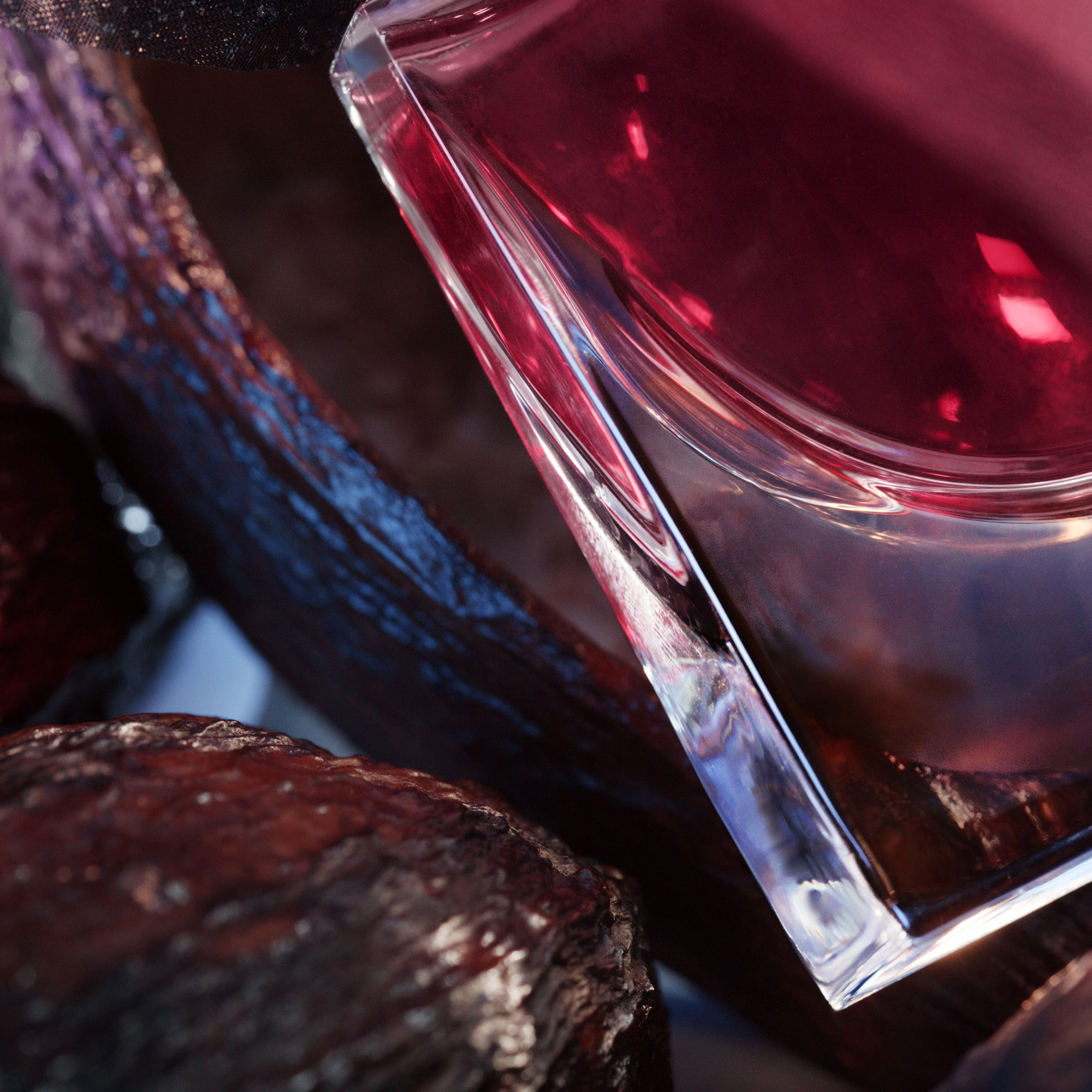 Close-up of a crystal perfume bottle reflecting deep hues, set against textured, dark stones and a soft backdrop.
