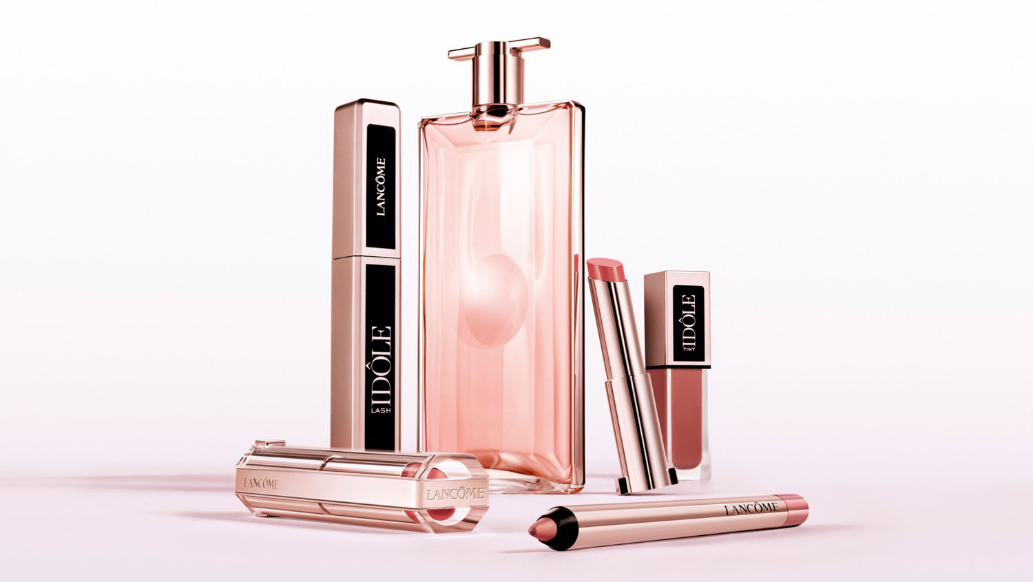 A collection of Lancôme’s Idôle fragrance and lip products displayed elegantly against a soft pink background.